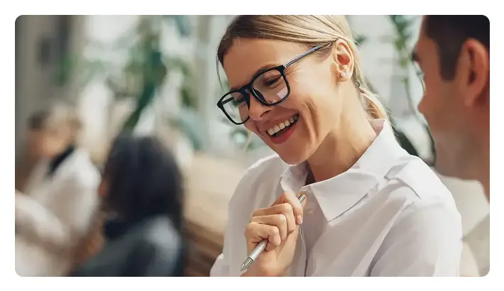 A professional woman with glasses is smiling while holding a pen